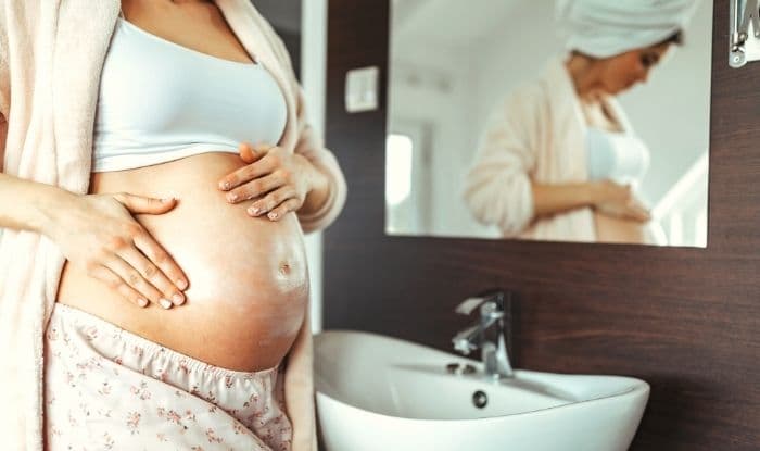 Mujer embarazada en el baño poniéndose crema para las estrias en la barriga.